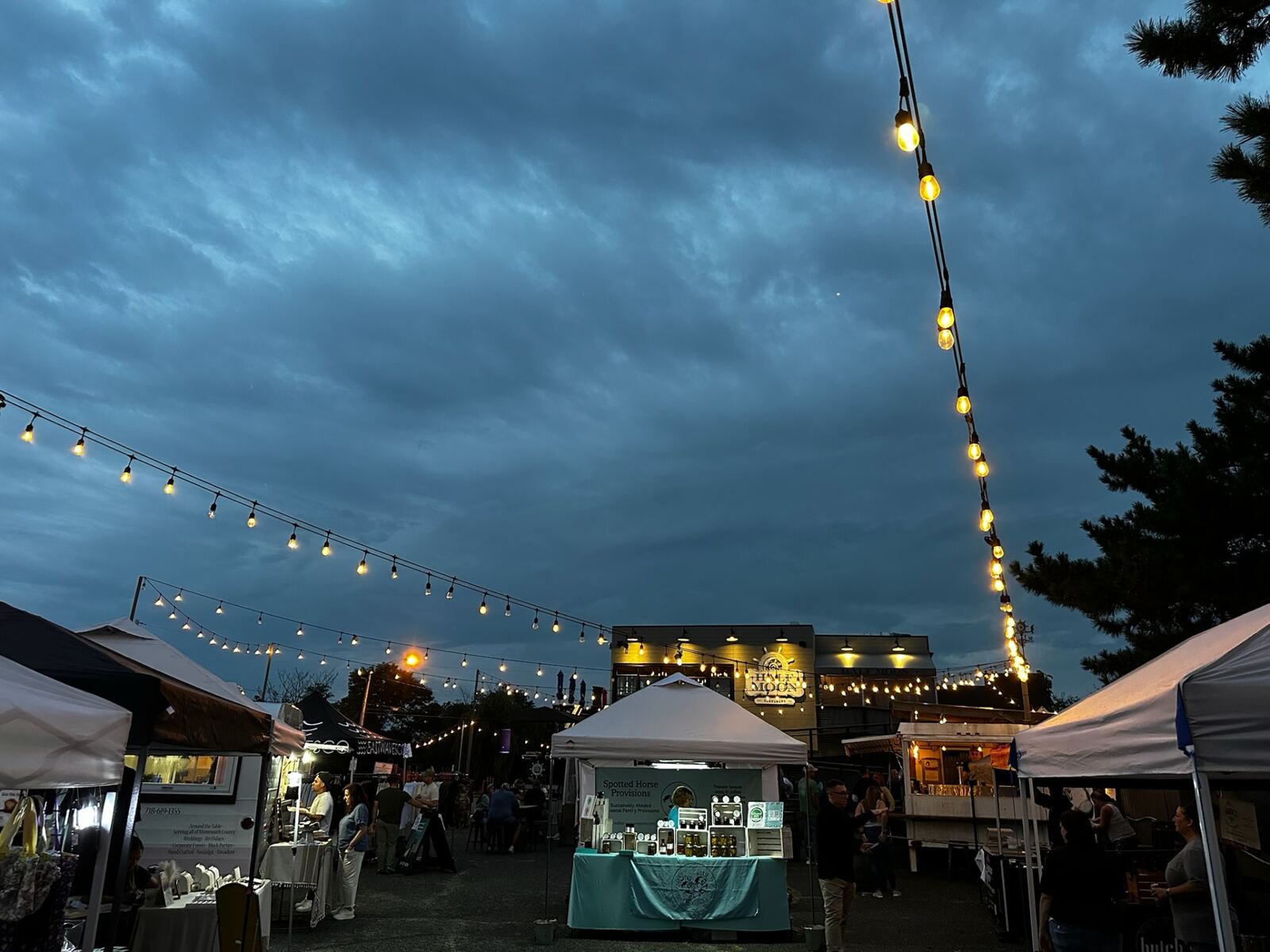 String lights against the dusk sky over the market with Half Moon glowing in the background